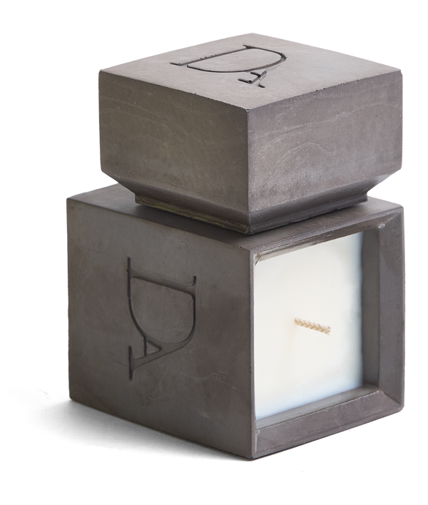 4oz Devetu artisanal candle in Apollo, encased in gunmetal black concrete square vessel with a lid. The lid, featuring the embossed 'DA' Devetu Aroma logo, adds a sleek finish to the candle's modern aesthetic.