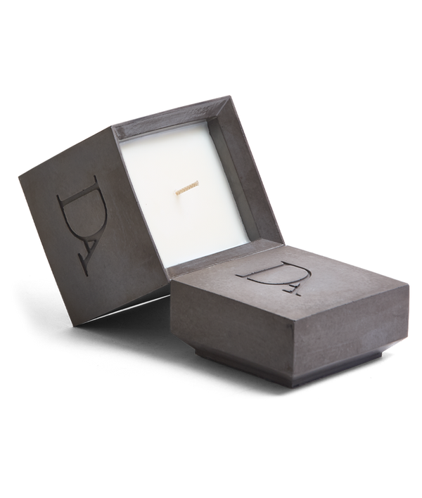 9oz Devetu artisanal candle in Apollo, encased in gunmetal black concrete square vessel with a lid. The lid, featuring the embossed 'DA' Devetu Aroma logo, adds a sleek finish to the candle's modern aesthetic.