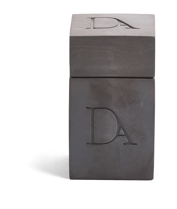 4oz Devetu artisanal candle in Apollo, encased in gunmetal black concrete square vessel with a lid. The lid, featuring the embossed 'DA' Devetu Aroma logo, adds a sleek finish to the candle's modern aesthetic.