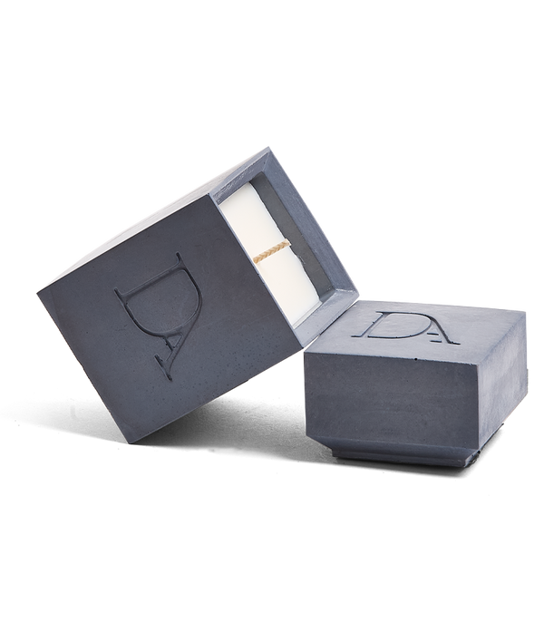 4oz Devetu artisanal candle in Elysian, encased in deep navy concrete square vessel with a lid. The lid, featuring the embossed 'DA' Devetu Aroma logo, adds a sleek finish to the candle's modern aesthetic.