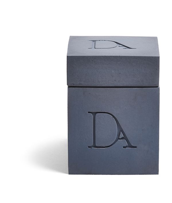 9oz Devetu artisanal candle in Elysian, encased in deep navy concrete square vessel with a lid. The lid, featuring the embossed 'DA' Devetu Aroma logo, adds a sleek finish to the candle's modern aesthetic.
