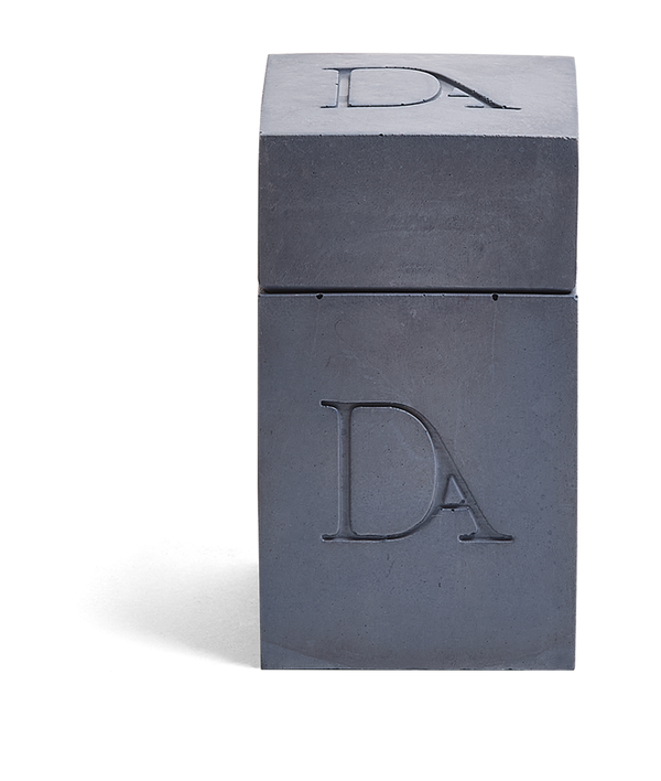 4oz Devetu artisanal candle in Elysian, encased in deep navy concrete square vessel with a lid. The lid, featuring the embossed 'DA' Devetu Aroma logo, adds a sleek finish to the candle's modern aesthetic.