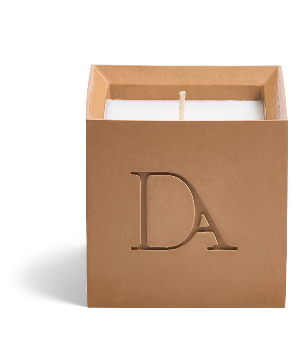 9oz Devetu artisanal candle in Embrace, crafted in a warm cashew colored concrete square vessel. The candle is uncovered, displaying the richly textured wax surface, with the 'DA' Devetu Aroma logo embossed on the front.