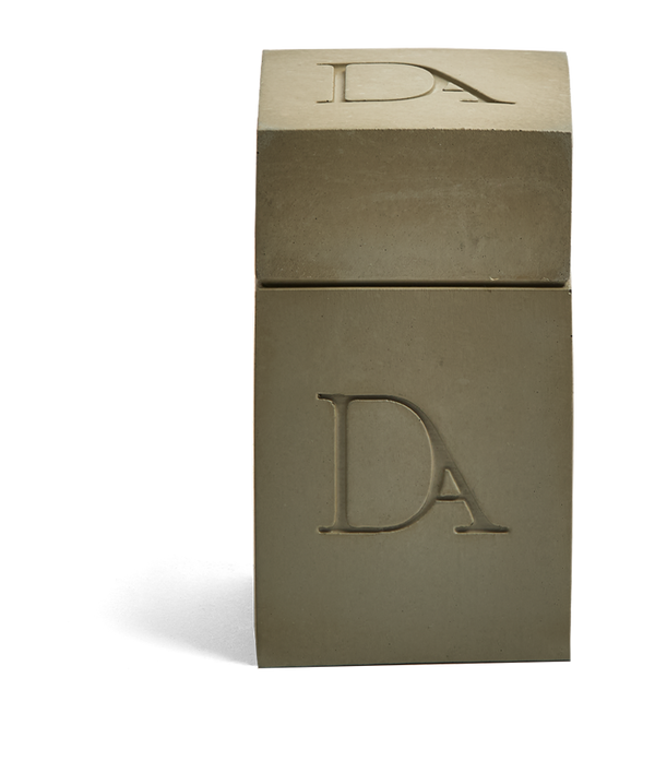 4oz Devetu artisanal candle in Wild Nomad, encased in deep olive green concrete square vessel with a lid. The lid, featuring the embossed 'DA' Devetu Aroma logo, adds a sleek finish to the candle's modern aesthetic.
