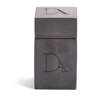 4oz Devetu artisanal candle in Apollo, encased in gunmetal black concrete square vessel with a lid. The lid, featuring the embossed 'DA' Devetu Aroma logo, adds a sleek finish to the candle's modern aesthetic.