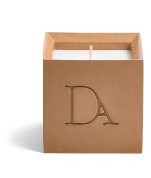 9oz Devetu artisanal candle in Embrace, crafted in a warm cashew colored concrete square vessel. The candle is uncovered, displaying the richly textured wax surface, with the 'DA' Devetu Aroma logo embossed on the front.