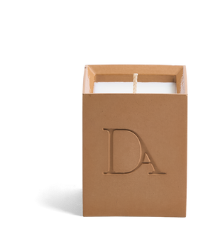 4oz Devetu artisanal candle in Embrace, crafted in a warm cashew colored concrete square vessel. The candle is uncovered, displaying the richly textured wax surface, with the 'DA' Devetu Aroma logo embossed on the front.