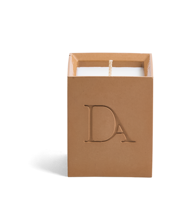 4oz Devetu artisanal candle in Embrace, crafted in a warm cashew colored concrete square vessel. The candle is uncovered, displaying the richly textured wax surface, with the 'DA' Devetu Aroma logo embossed on the front.