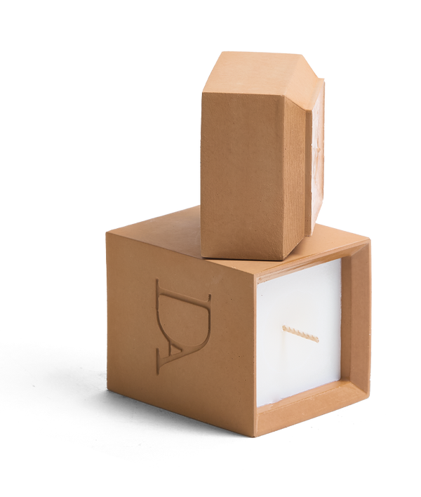 4oz Devetu artisanal candle in Embrace, encased in warm cashew colored concrete square vessel with a lid. The lid, featuring the embossed 'DA' Devetu Aroma logo, adds a sleek finish to the candle's modern aesthetic.