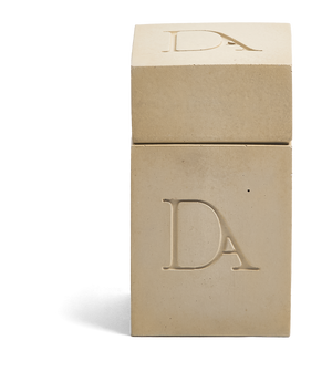 4oz Devetu artisanal candle in Gravity, encased in soft taupe concrete square vessel with a lid. The lid, featuring the embossed 'DA' Devetu Aroma logo, adds a sleek finish to the candle's modern aesthetic.