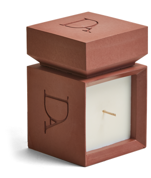 9oz Devetu artisanal candle in Phoenix, encased in burnt red concrete square vessel with a lid. The lid, featuring the embossed 'DA' Devetu Aroma logo, adds a sleek finish to the candle's modern aesthetic.