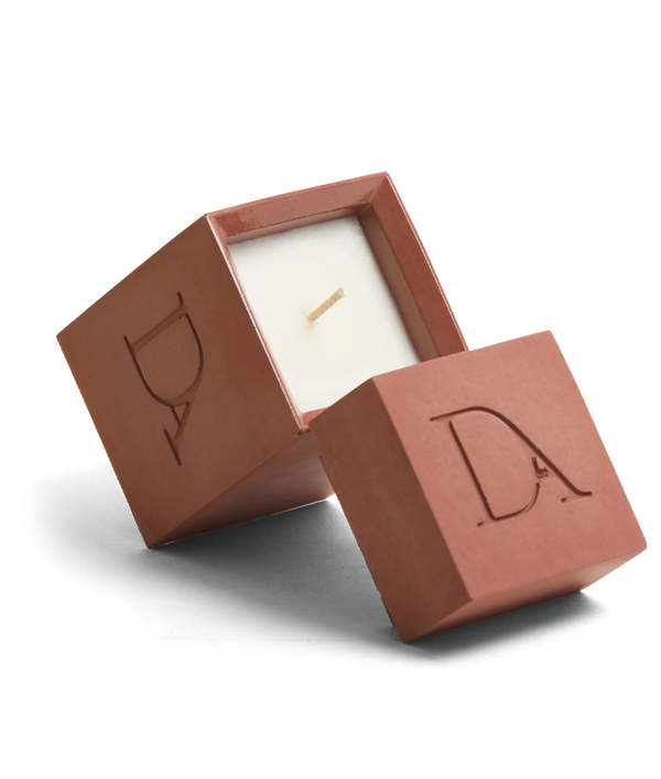 4oz Devetu artisanal candle in Phoenix, encased in burnt red concrete square vessel with a lid. The lid, featuring the embossed 'DA' Devetu Aroma logo, adds a sleek finish to the candle's modern aesthetic.