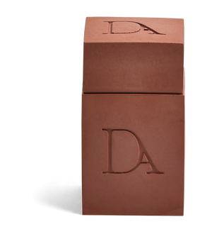 4oz Devetu artisanal candle in Phoenix, encased in burnt red  concrete square vessel with a lid. The lid, featuring the embossed 'DA' Devetu Aroma logo, adds a sleek finish to the candle's modern aesthetic.