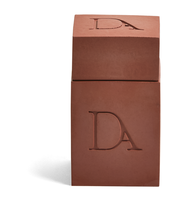 4oz Devetu artisanal candle in Phoenix, encased in burnt red  concrete square vessel with a lid. The lid, featuring the embossed 'DA' Devetu Aroma logo, adds a sleek finish to the candle's modern aesthetic.