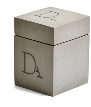 9oz Devetu artisanal candle in Odyssey, encased in ash grey concrete square vessel with a lid. The lid, featuring the embossed 'DA' Devetu Aroma logo, adds a sleek finish to the candle's modern aesthetic.